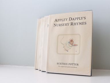 A stack of books with the top one titled Appley Dapply's Nursery Rhymes by Beatrix Potter on a white surface