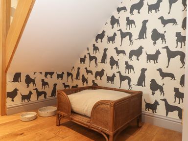 A corner with a wicker dog bed and two bowls on a wooden floor and dog silhouette wallpaper at The Riblows Cape Cornwall in Bollowal near St Just