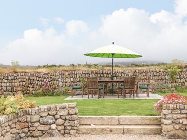 An outdoor patio area with a wooden table and chairs under a green umbrella in a garden surrounded by stone walls at The Riblows Cape Cornwall in Bollowal near St Just