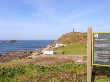 A coastal landscape with buildings near the ocean and a hill with a chimney stack at Cape Cornwall Bollowal near St Just