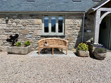 A wooden bench on a stone patio against a stone wall with plants in stone and ceramic pots at The Riblows Cape Cornwall in Bollowal near St Just
