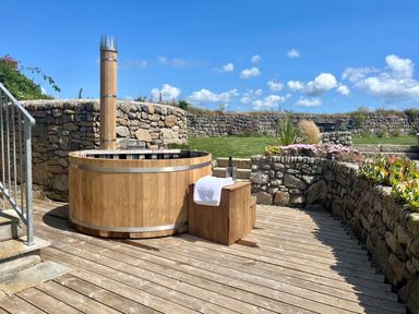 An outdoor wooden hot tub on a wooden deck with stone walls and garden plants at The Riblows Cape Cornwall Bollowal near St Just