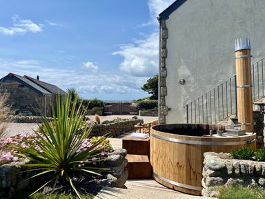 An outdoor wooden hot tub next to a wall with stairs and stone planters with plants and flowers at The Riblows  Cape Cornwall Bollowal near St Just
