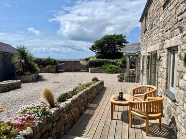 A stone patio with wooden chairs and table overlooking a gravel yard with plants and a wooden gate at The Riblows Cape Cornwall in Bollowal near St Just