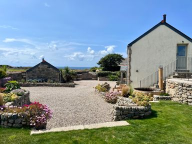 An outdoor area with gravel paths stone flower beds and two buildings under a blue sky at The Riblows Cape Cornwall in Bollowal near St Just
