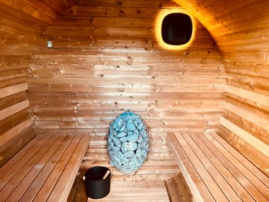 An interior of a sauna with wooden benches a heater with stones and a black bucket at The Riblows Cape Cornwall in Bollowal near St Just