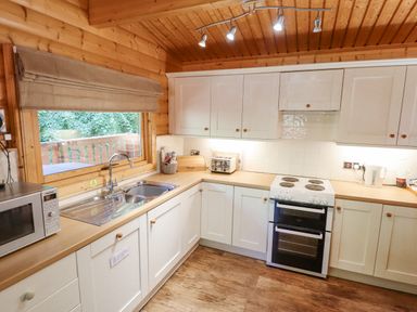 A kitchen with white cabinets a stove a sink microwave and a window with a view of trees at 64 Acorn Lodge Kenwick Park in Louth