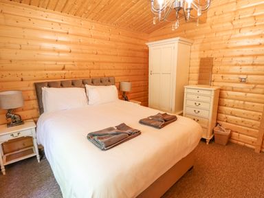 A bedroom with a double bed white bedding two bedside tables with lamps a wardrobe and a chest of drawers at 64 Acorn Lodge Kenwick Park Louth