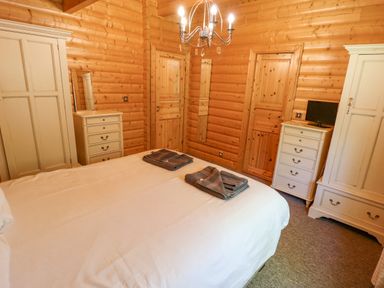 A bedroom with a bed towels two wardrobes two dressers a small television and wooden walls at 64 Acorn Lodge Kenwick Park Louth