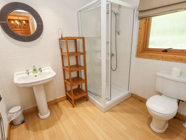 A bathroom with a pedestal sink a shower cubicle a wooden shelving unit a toilet and a window at 64 Acorn Lodge Kenwick Park in Louth
