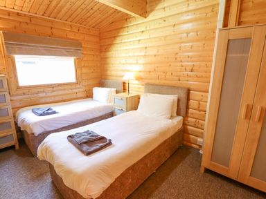 A bedroom with two single beds a nightstand with a lamp and a wardrobe in 64 Acorn Lodge Kenwick Park Louth