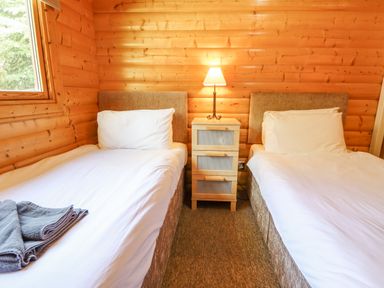 A bedroom with two single beds separated by a nightstand with a lamp in a wooden cabin at 64 Acorn Lodge Kenwick Park in Louth