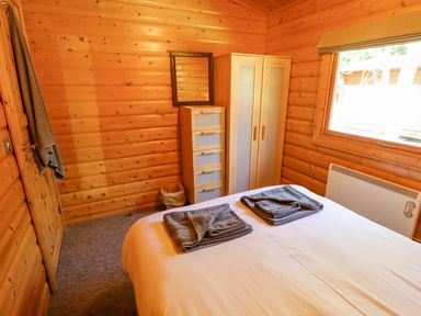 A bedroom with wooden walls a bed with folded towels a chest of drawers and a wardrobe at 64 Acorn Lodge Kenwick Park in Louth