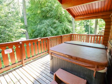 A wooden balcony with a covered hot tub and railing surrounded by trees at 64 Acorn Lodge Kenwick Park in Louth