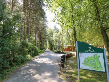 A paved path surrounded by tall trees and dense greenery with a map sign for The Woods on the right side at 64 Acorn Lodge Kenwick Park in Louth