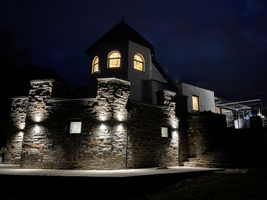 A stone wall with lights and a house with lit windows at night at Glamorgan House in Cardiff