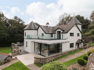 A white two-story house with two turrets glass balcony and stone walls surrounded by grass and trees at Glamorgan House in Cardiff
