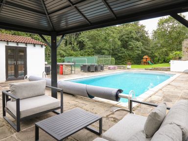 An outdoor swimming pool with patio furniture under a covered seating area and a small building near the pool at Glamorgan House in Cardiff