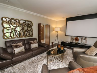 A living room with brown leather sofa and armchairs a decorative mirror a floor lamp a glass coffee table and a wall-mounted projector screen at Glamorgan House in Cardiff