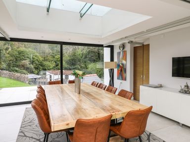 A dining room with a large wooden table surrounded by brown chairs and a vase with flowers at Glamorgan House Cardiff