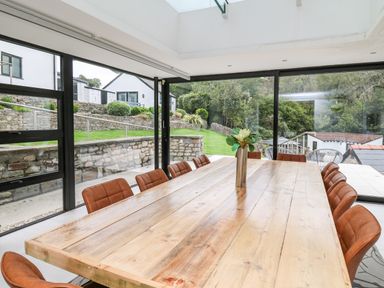 A dining area with a wooden table and brown chairs next to large windows showing a garden at Glamorgan House in Cardiff