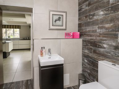 A small bathroom with a sink cabinet and toilet next to a door leading to a kitchen with white cabinets at Glamorgan House in Cardiff