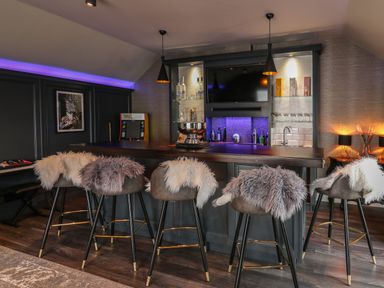 A bar area with six stools covered in fur throws a television and shelves with bottles behind Glamorgan House Cardiff