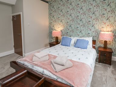 A bedroom with a double bed two bedside tables with lamps folded towels and floral wallpaper at Glamorgan House in Cardiff