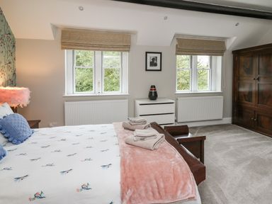 A bedroom with a bed with folded towels a white dresser two windows and a wooden wardrobe at Glamorgan House in Cardiff