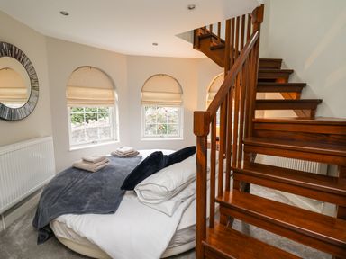 A bedroom with a round bed near three arched windows and a wooden staircase at Glamorgan House in Cardiff