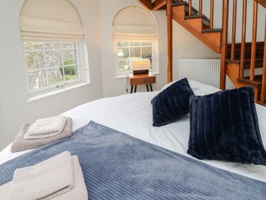 A bedroom with a bed with navy pillows and folded towels next to wooden stairs and two windows at Glamorgan House in Cardiff