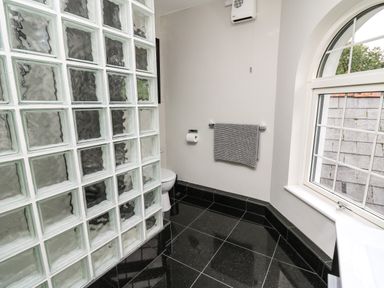 A bathroom with a glass block shower wall toilet towel rack and arched window at Glamorgan House in Cardiff