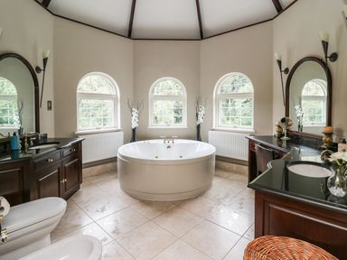 A bathroom with a central round bathtub two dark wood vanities with mirrors and sinks and three arched windows at Glamorgan House in Cardiff