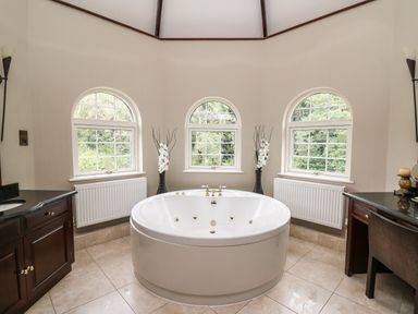 A bathroom with a large round bathtub between three arched windows and two dark wooden vanities at Glamorgan House in Cardiff