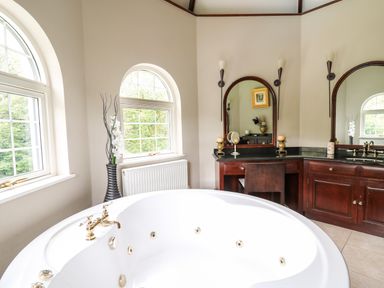 A bathroom with a large round bathtub wooden vanity with two mirrors and windows showing greenery at Glamorgan House in Cardiff