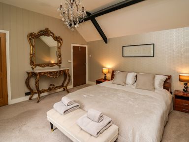 A bedroom with a large bed two bedside tables with lamps an ornate mirror and table a chandelier and a padded bench with towels at Glamorgan House in Cardiff