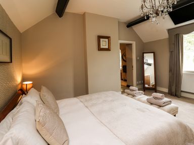 A bedroom with a bed with pillows and folded towels at the foot a floor mirror a window with curtains and a chandelier at Glamorgan House Cardiff