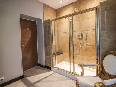 A bathroom with a glass shower enclosure wooden door and an ornate chair at Glamorgan House in Cardiff