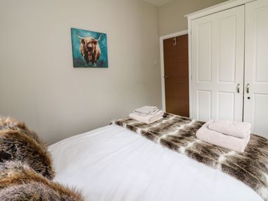 A bedroom with a bed with white sheets and fur throw towels on the bed a painting of a highland cow on the wall a wooden door and white wardrobe at Glamorgan House in Cardiff