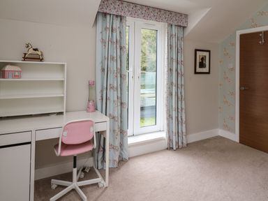 A room with a white desk and pink chair next to glass doors with floral curtains at Glamorgan House in Cardiff