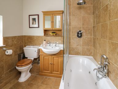 A bathroom with a toilet and wooden cabinet with sink next to a bathtub with a shower at Glamorgan House in Cardiff