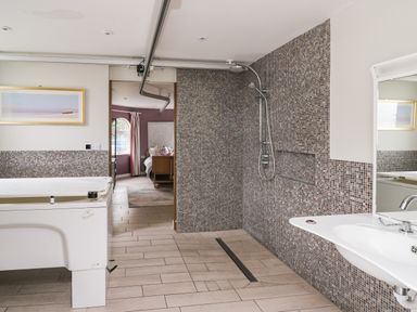 A bathroom with a walk-in shower a sink and a white bathtub with a door open to a bedroom at Glamorgan House in Cardiff