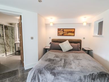 A bedroom with a bed gray bedding two small side tables and a bathroom with glass shower doors at Glamorgan House in Cardiff