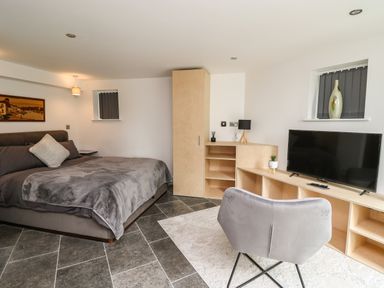 A bedroom with a bed grey bedding a chair and a television on a wooden unit at Glamorgan House in Cardiff
