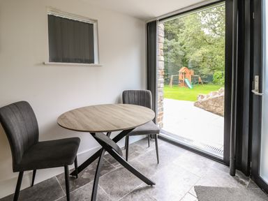 A small dining area with a round table and two chairs next to a glass door overlooking a garden with a play structure at Glamorgan House in Cardiff