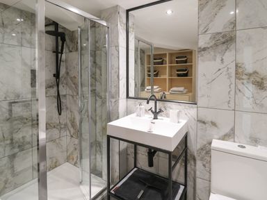 A bathroom with a shower, sink with faucet and mirror, shelving with towels and baskets at Glamorgan House in Cardiff