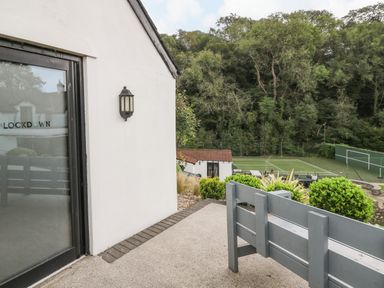 A patio area with a bench and wall light overlooking a sports court and trees at Glamorgan House in Cardiff