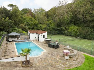 An outdoor area with a swimming pool tennis court dining table and seating at Glamorgan House Cardiff