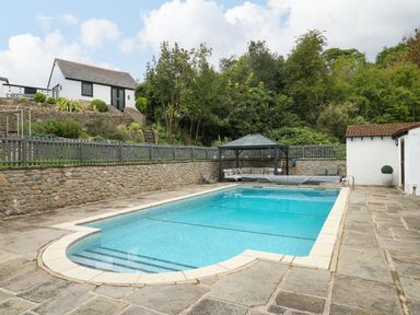 An outdoor swimming pool with poolside seating and a small building near trees and a stone wall at Glamorgan House in Cardiff