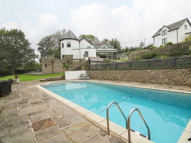 An outdoor swimming pool with stone patio and loungers near a white house with castle-like features and turrets at Glamorgan House in Cardiff